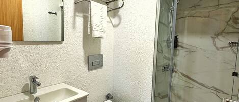 A bathroom with a marble shower, a sink, a toilet, and a mirror.