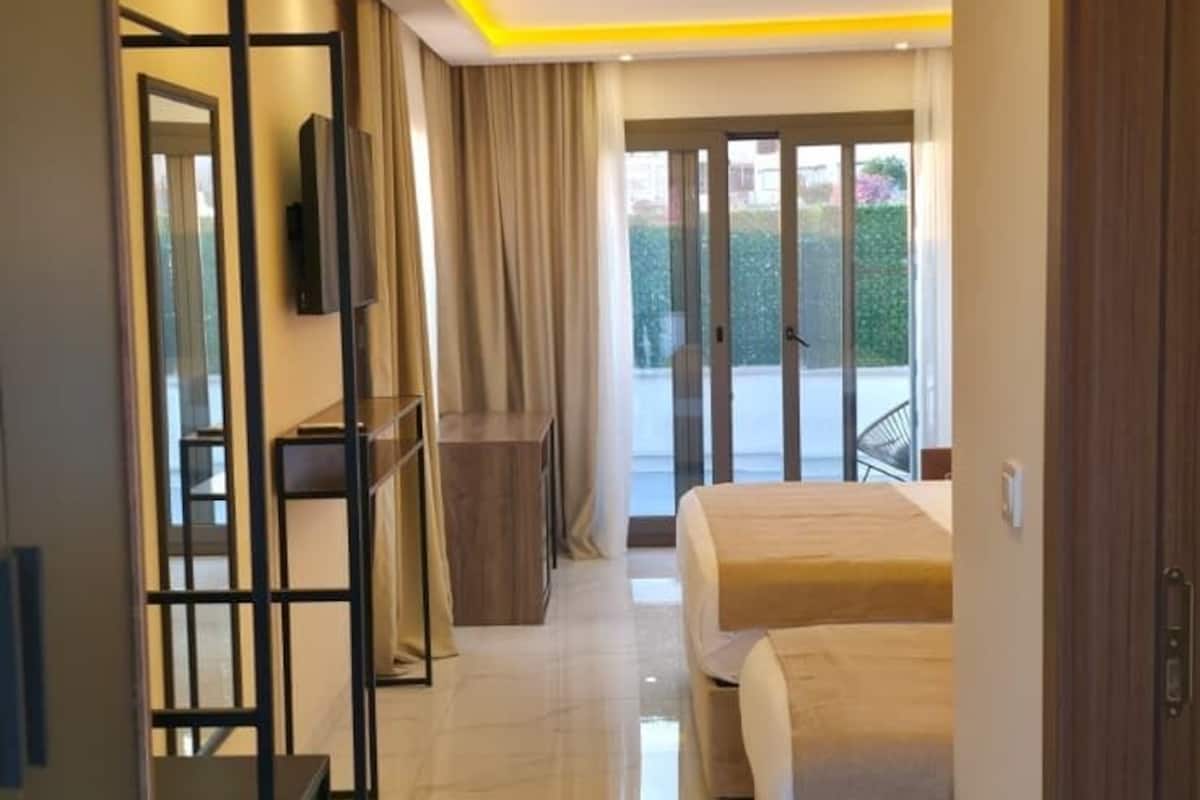 Quarto de hotel moderno com uma cama grande, televisão, guarda-roupa e varanda com vista.