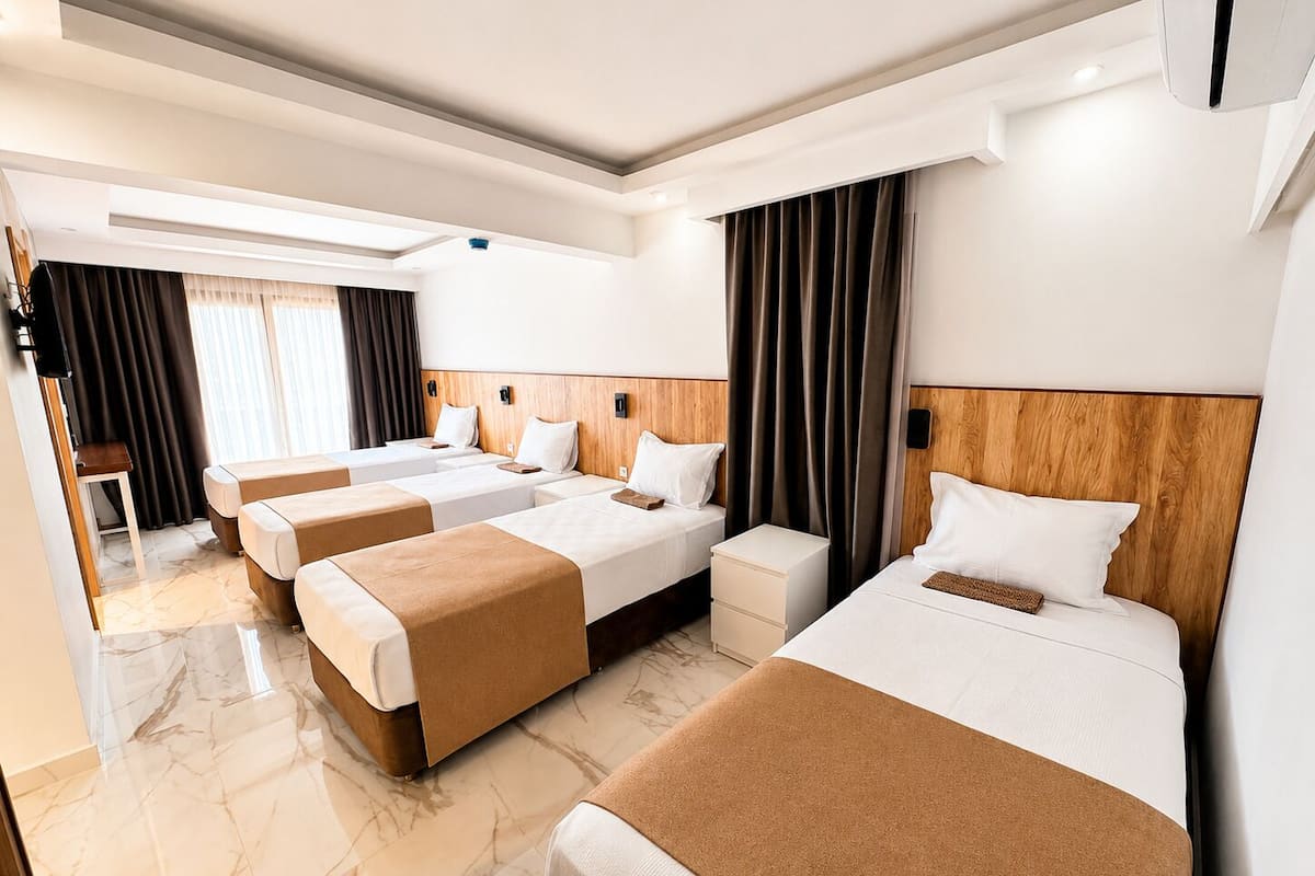 A hotel room with three beds, a wooden headboard, a marble floor, and a television on the left.