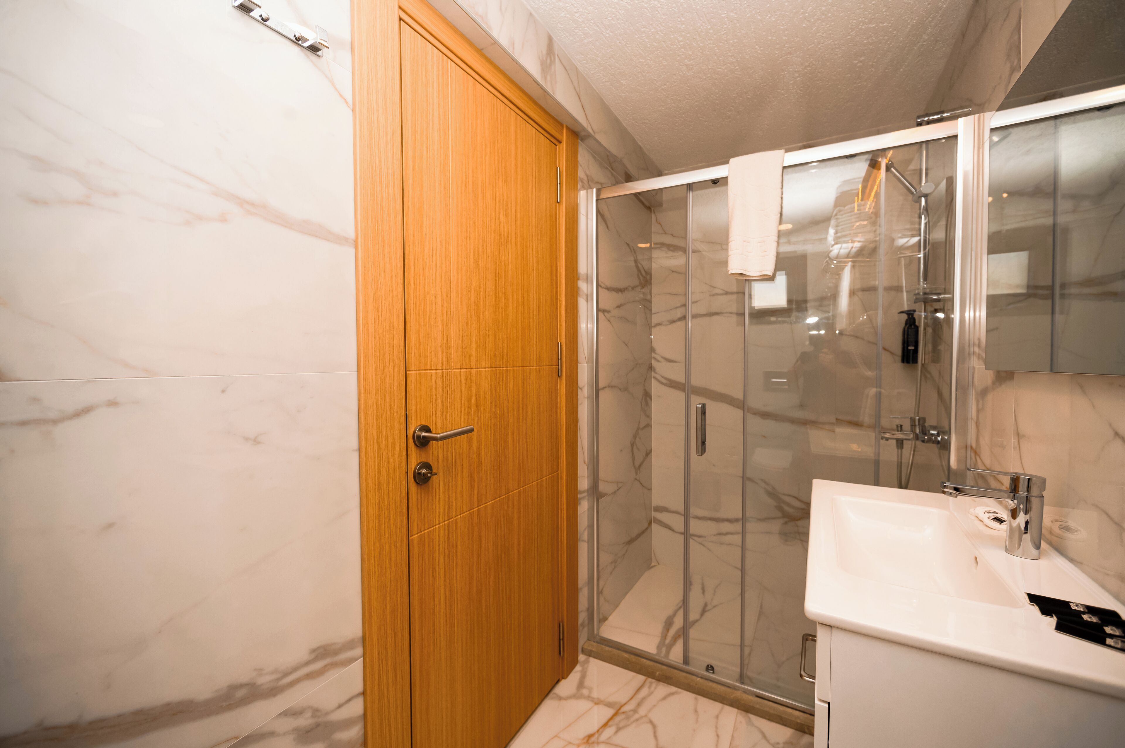 A bathroom with a wooden door, a glass shower enclosure, and a white sink.