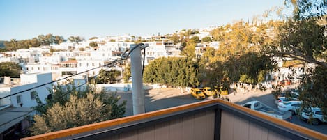 A view from a balcony overlooking a residential area with white buildings, a street with cars, and a tall utility pole.