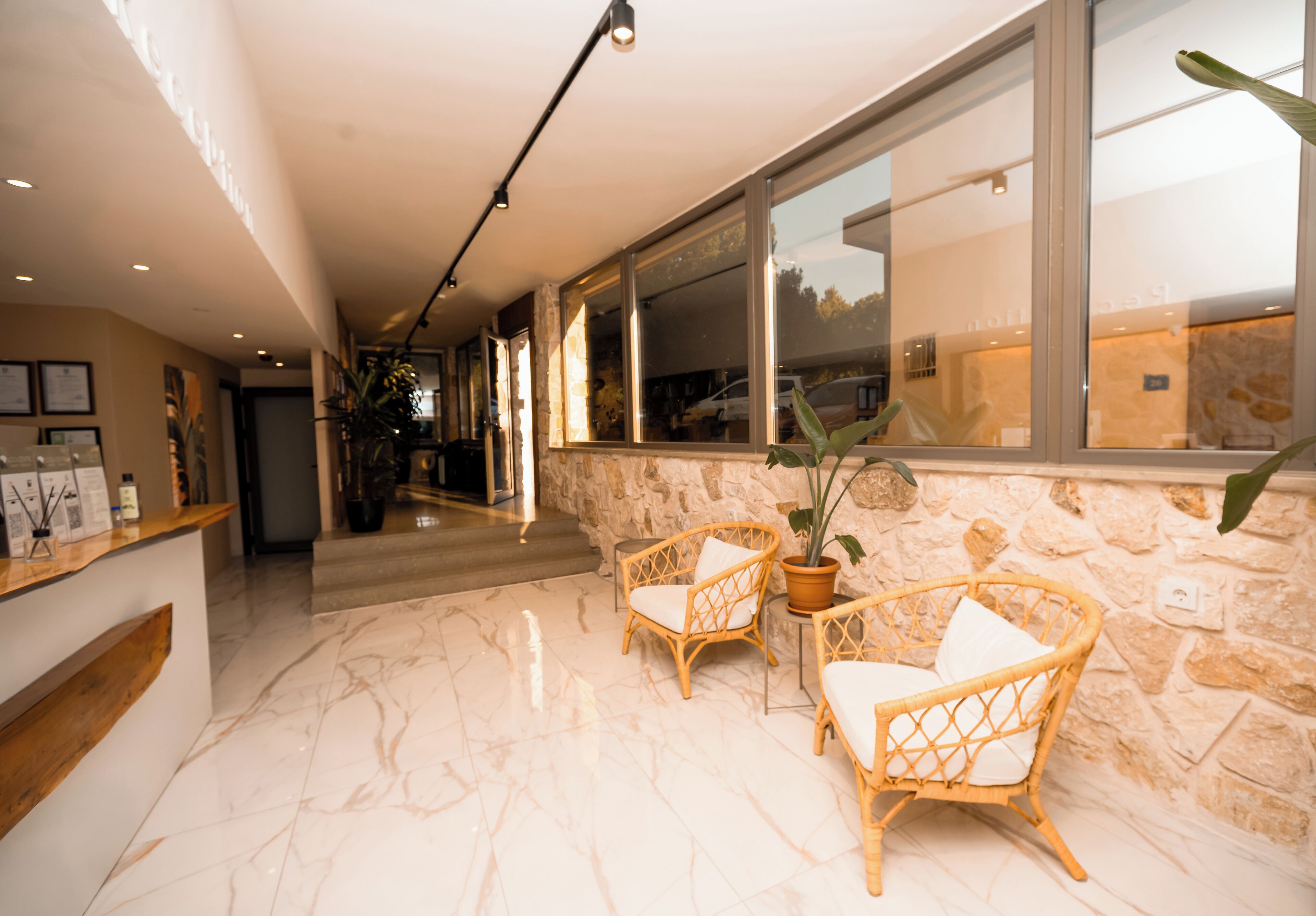 Un área de recepción con piso de mármol, sillas de mimbre, un mostrador de recepción y un gran ventanal con vistas al exterior.