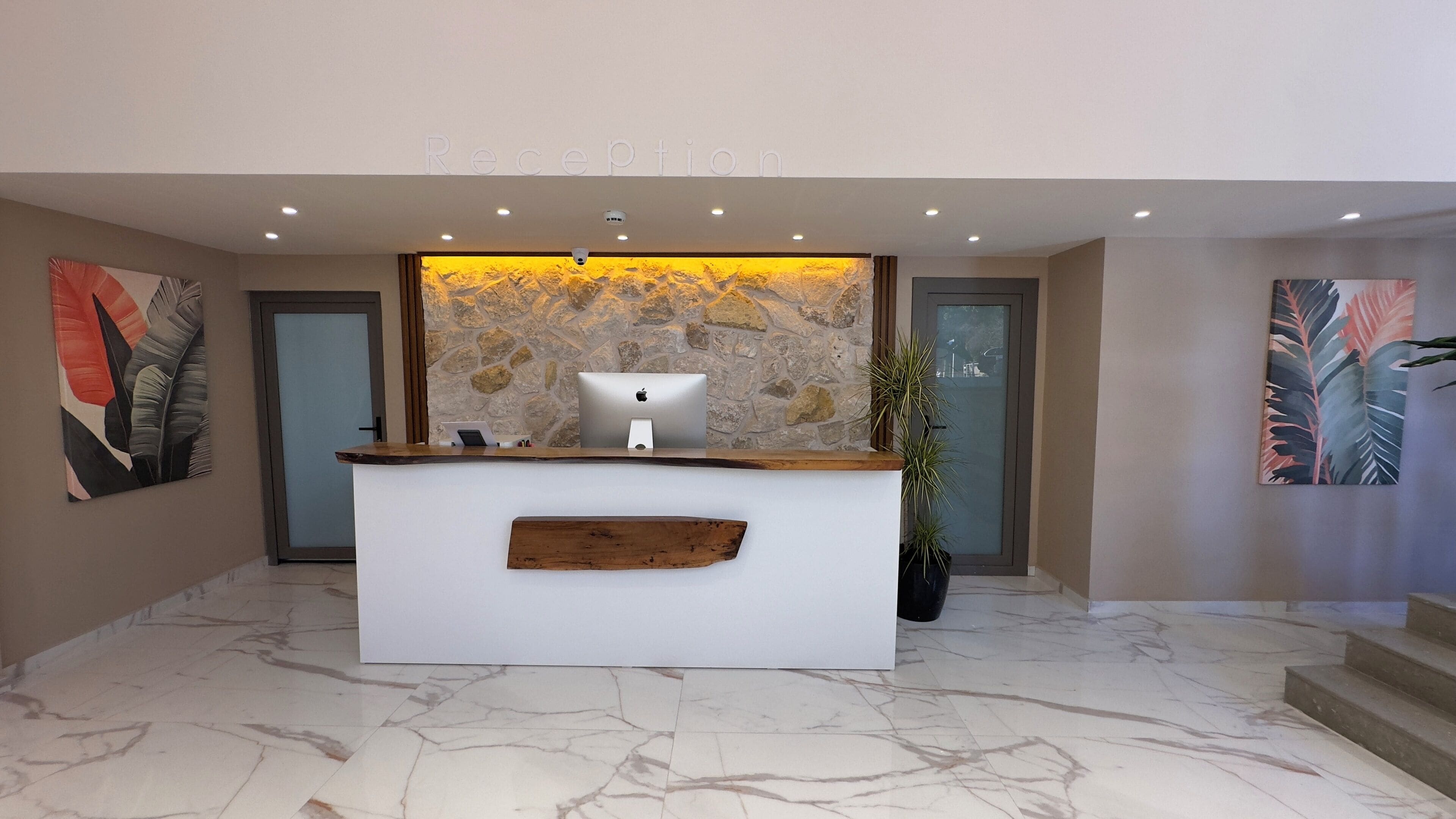 A reception desk with a stone wall backdrop, a laptop, and a plant.