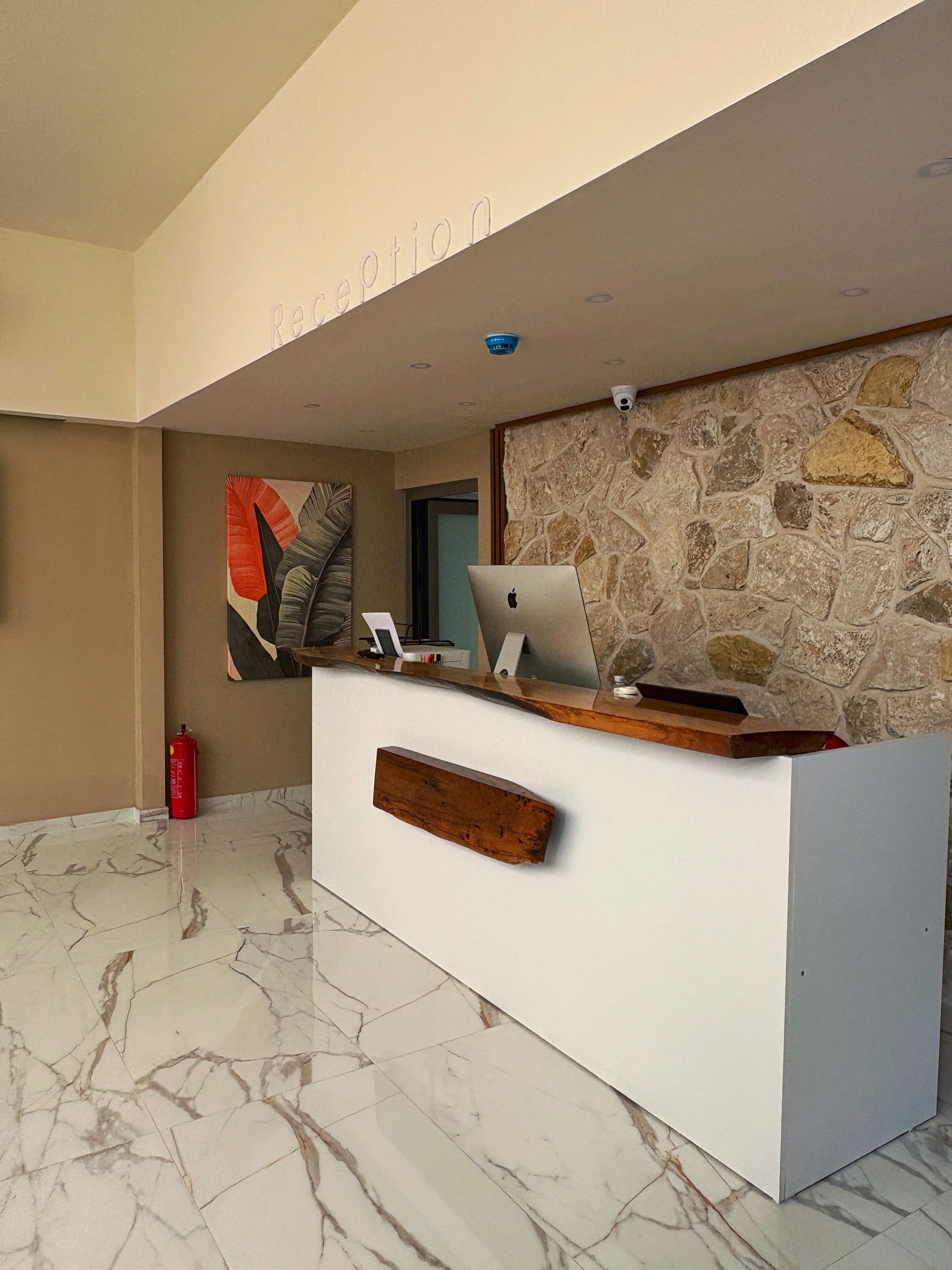 A reception desk with a laptop, a fire extinguisher, and a stone wall.