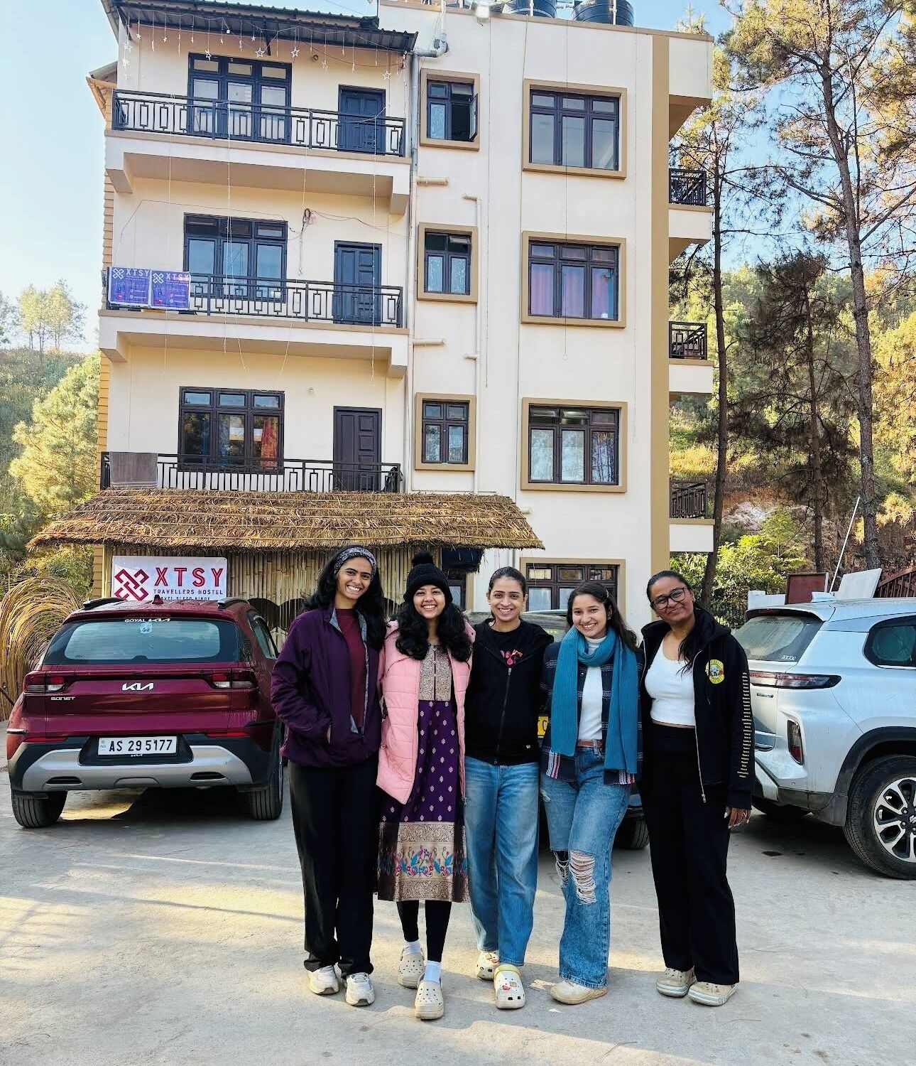 Un groupe de personnes se tient devant un immeuble doté de balcons et d’une enseigne indiquant « XTSY TRAVELERS HOSTEL ».