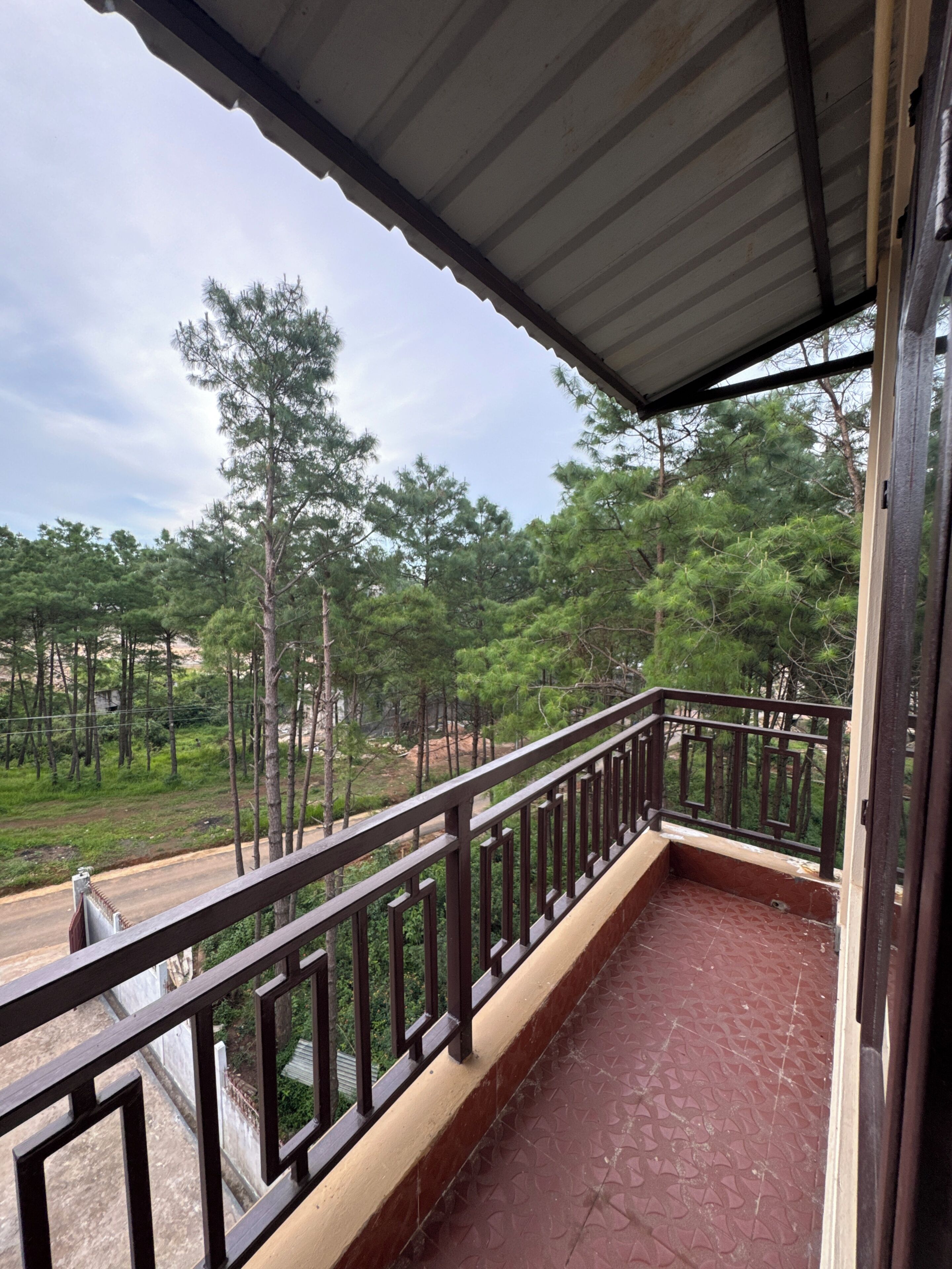 A balcony with a metal railing, a tiled floor, and a view of a forested area.