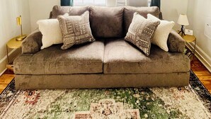A living room with a grey sofa, patterned cushions, a patterned rug, and a window with curtains. - Charming 1-bedroom condo that sleeps 4 in enchanting Savannah on Historic Square (Savannah)