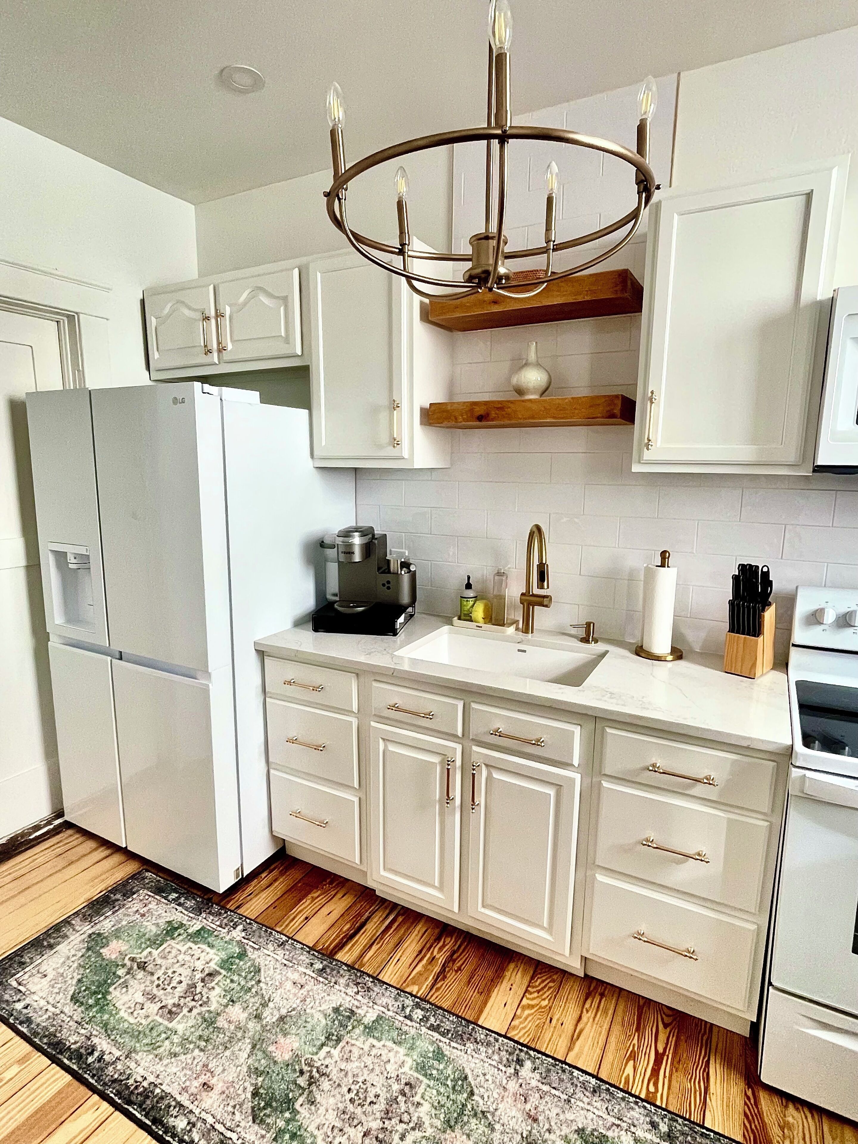 A kitchen with white cabinets, a refrigerator, a sink, a stove, and a chandelier.