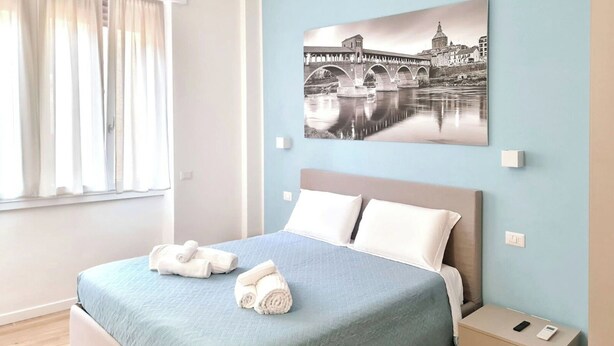 Una camera d'albergo moderna con un letto, un comodino e un quadro appeso al muro raffigurante un ponte.