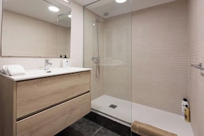 A modern bathroom with a glass shower enclosure, a wooden vanity, and a large mirror.