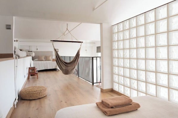A spacious room with a hanging chair, a bed with rolled towels, a small stool, and a large window with a grid pattern.