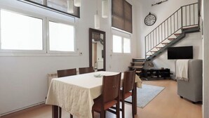Un comedor con una mesa, sillas, una escalera, un reloj y un televisor.