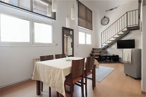 A dining area with a table and chairs, a staircase, a clock, and a television.