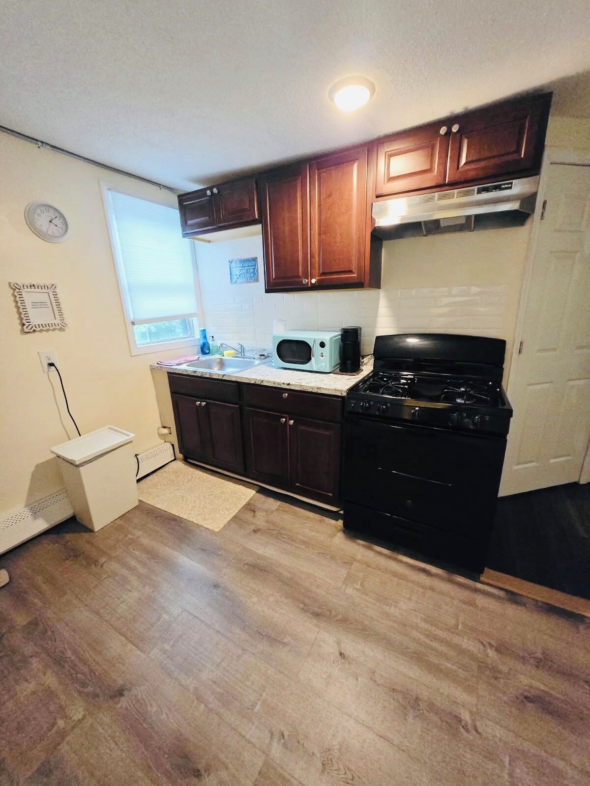 A kitchen with wooden cabinets, a microwave, a stove, a small refrigerator, and a window.