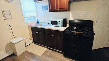 A kitchen with wooden cabinets, a microwave, a stove, a small refrigerator, and a window.