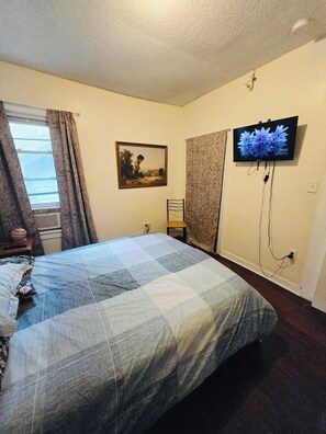 A bedroom with a bed, a painting, a television, and a window with curtains.