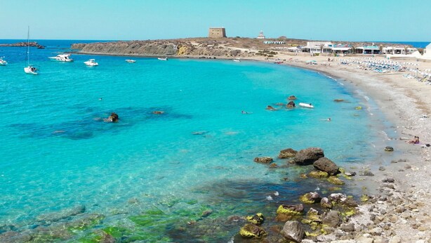 A coastal beach with clear turquoise waters, rocky shoreline, and a historic building in the background. - Alicante Vacation Home (Gran Alacant)