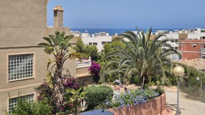 A residential area with a view of the sea, featuring a building with a balcony, lush greenery, and a clear sky. - Alicante Vacation Home (Gran Alacant)