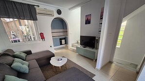 A modern living room with a sectional sofa, a small white table, and a TV on a cabinet. - Alicante Vacation Home (Gran Alacant)