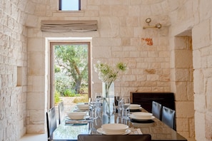 A dining area with a stone wall, a large window, and a table set for a meal. - Belmont Trulli – A Sanctuary of Timeless Luxury (Carovigno)
