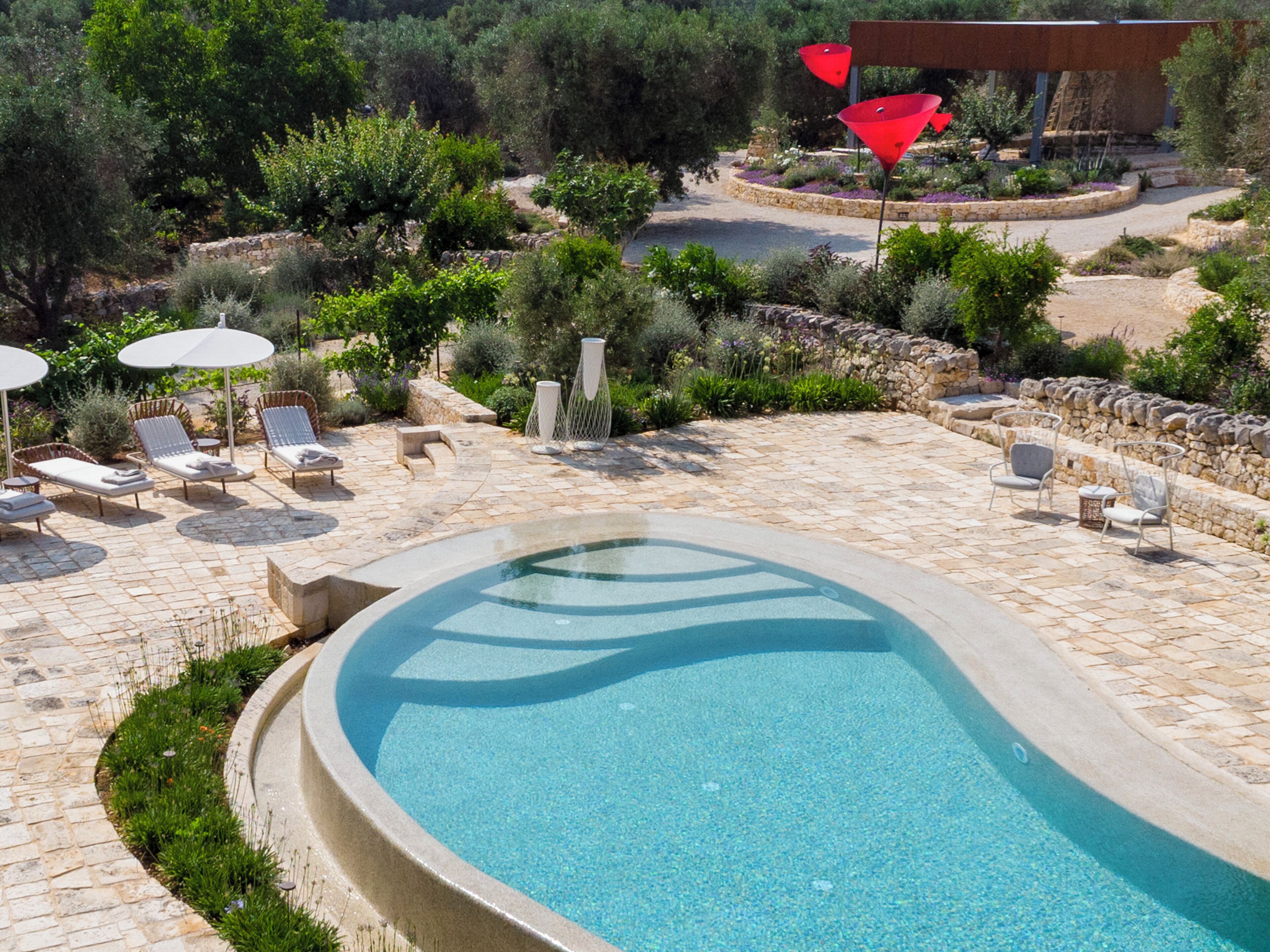 A swimming pool with lounge chairs and umbrellas, surrounded by stone walls and greenery.
