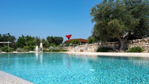 Une piscine aux eaux cristallines, bordée d’un mur en pierre et dotée de chaises longues.