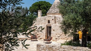 Un edificio de piedra con techo cónico, dos zonas de estar al aire libre y un camino de piedra que conduce a la entrada.