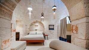 Un dormitorio con pared de piedra, una cama, un banco y luces colgantes.