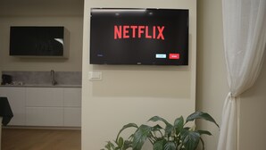 A modern living room with a mounted TV displaying 'NETFLIX' and a kitchen area with white cabinets and a sink. - The Prince's Palace, a historic mansion (Abruzzo)