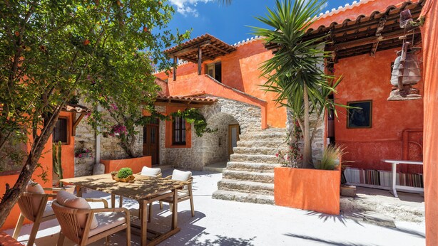 An outdoor patio with a wooden table and chairs, surrounded by orange walls and stone steps. - Old Town Charm – Casa Historica (Ermioni)