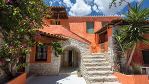 A stone building with a staircase leading to a door, surrounded by potted plants and flowering trees. - Old Town Charm – Casa Historica (Ermioni)