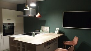 Une cuisine moderne dotée d’un îlot central, de luminaires suspendus et d’un mur d’accent vert foncé.