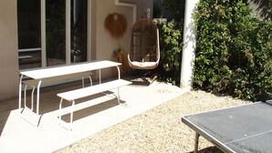 Une terrasse extérieure avec une table et des bancs, un fauteuil suspendu et une table de ping-pong.