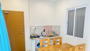 Eine kleine Küche mit Holztisch und -stühlen, einer kompakten Arbeitsplatte mit Spüle und einem Fenster mit Jalousien.