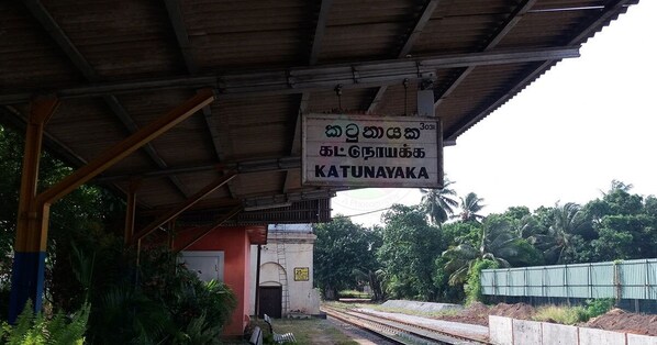 Estación de tren Katunayaka con un letrero en idioma local, un techo cubierto y vías.