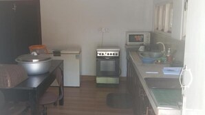 A compact kitchen with a stove, microwave, sink, and a small dining area with a table and chairs. - The Garden Resort Airport Katunayaka (Katunayake)