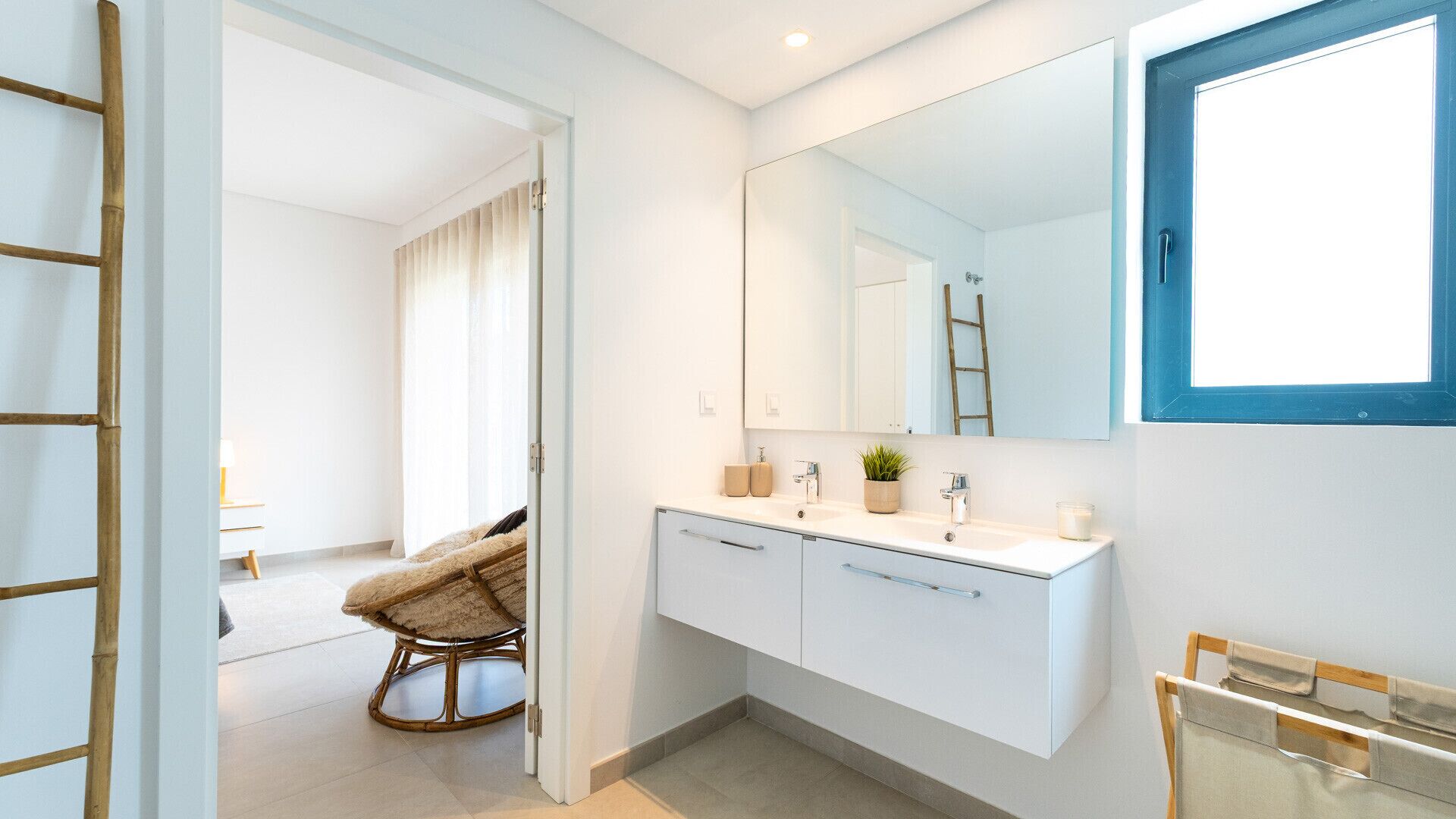 Une salle de bain moderne avec un grand miroir, des meubles blancs, un lavabo et une petite plante en pot.