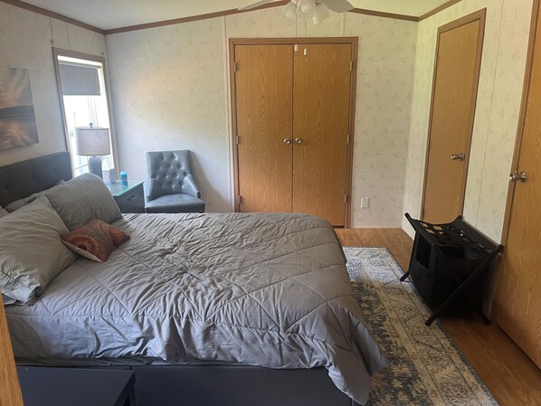 Un dormitorio con una cama grande, una silla, un armario y un escritorio con una lámpara.
