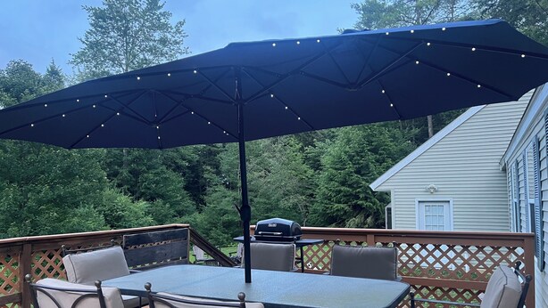 Eine Terrasse im Freien mit Tisch, Stühlen, einem Grill und einem großen Sonnenschirm.