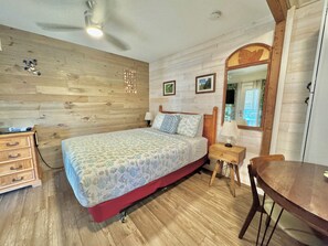 Une chambre à coucher avec une tête de lit en bois, un lit avec une literie à motifs, une table de chevet avec une lampe, une commode en bois et une table à manger.