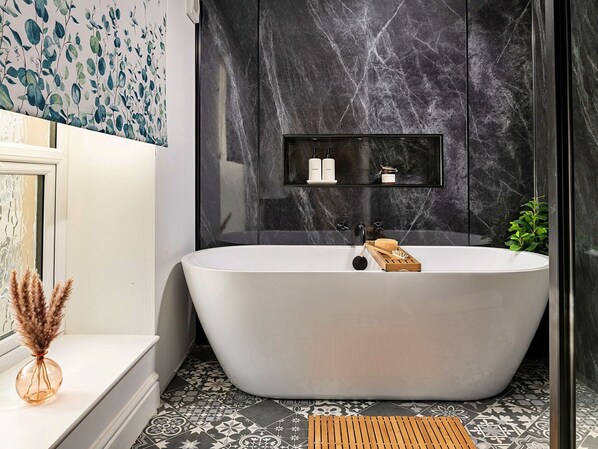 Un baño moderno con una bañera independiente, un pequeño estante con artículos de aseo y un piso estampado.