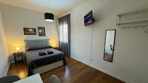 Camera d'albergo moderna con un letto, comodini, una scrivania, una sedia, una TV, uno specchio e una finestra con tende.