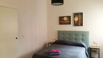 Un dormitorio con un cabecero tapizado de color verde, una cama con cubrecama oscuro, dos mesitas de noche y un cuadro abstracto en la pared.