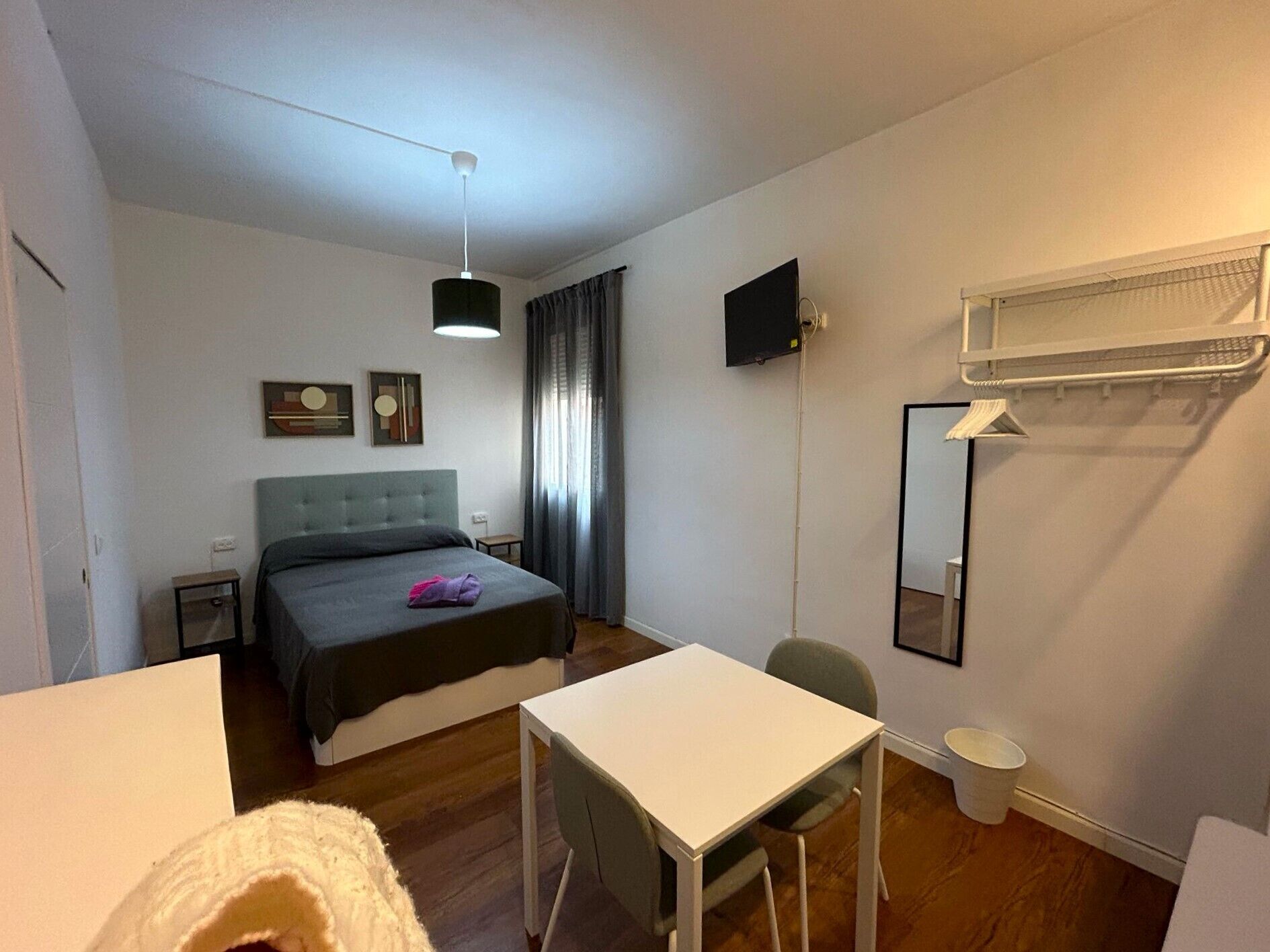 A bedroom with a bed, a desk, a chair, a television, and a window with curtains.