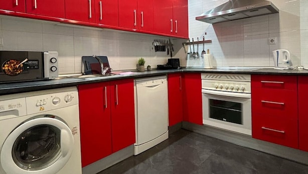 Una cucina moderna con pensili rossi, forno integrato, lavastoviglie e lavatrice.