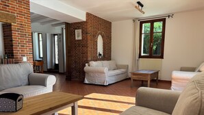 Amplia sala de estar con chimenea de ladrillo, dos sofás, una mesa de madera y una ventana con cortinas.
