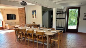 Un comedor con una mesa de madera dispuesta para seis personas, rodeada de sillas de madera, una pared de ladrillo y un televisor montado en la pared.