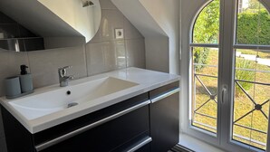 Un baño moderno con un lavamanos grande de color blanco, armarios oscuros y una ventana con vista a la vegetación.