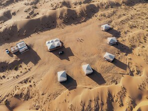 An aerial view of a desert campsite with multiple tents arranged in a semi-circle, surrounded by sand dunes. - Silent Dunes Camp (Bidiya)