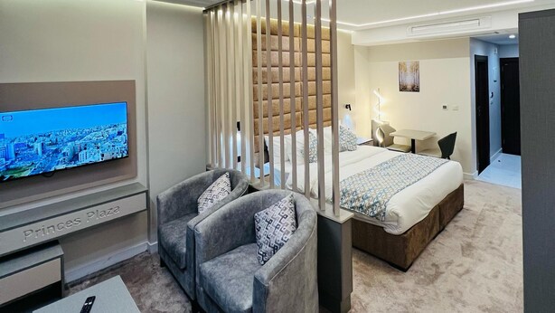 A modern hotel room with a large flat-screen TV, a sofa, a small table, and a bed with a headboard. - Princess Plaza hotel (Ma'an)